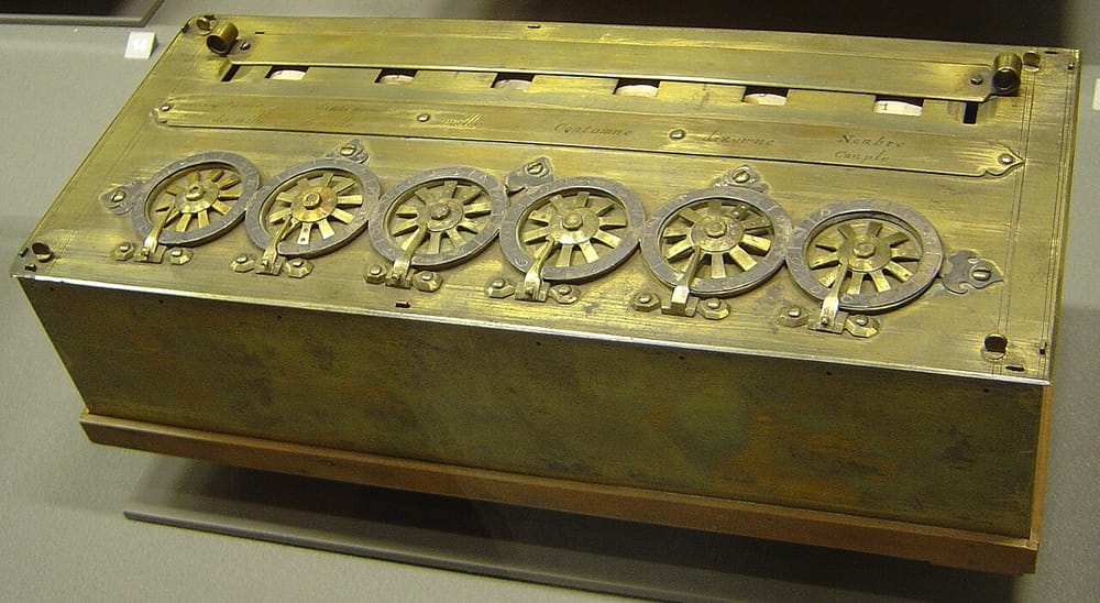 A Pascaline: a brass box with six toothed wheels on top, each with a small metal stop.