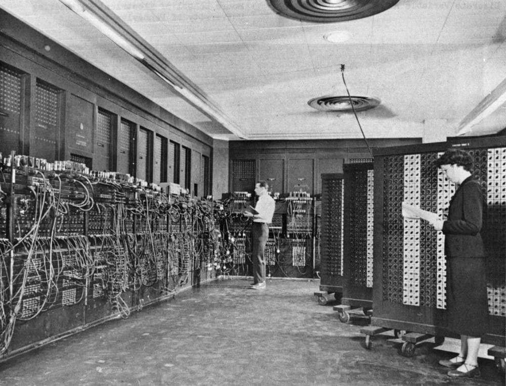 ENIAC: tall panels covered in plugged-in cables, and two people at work.