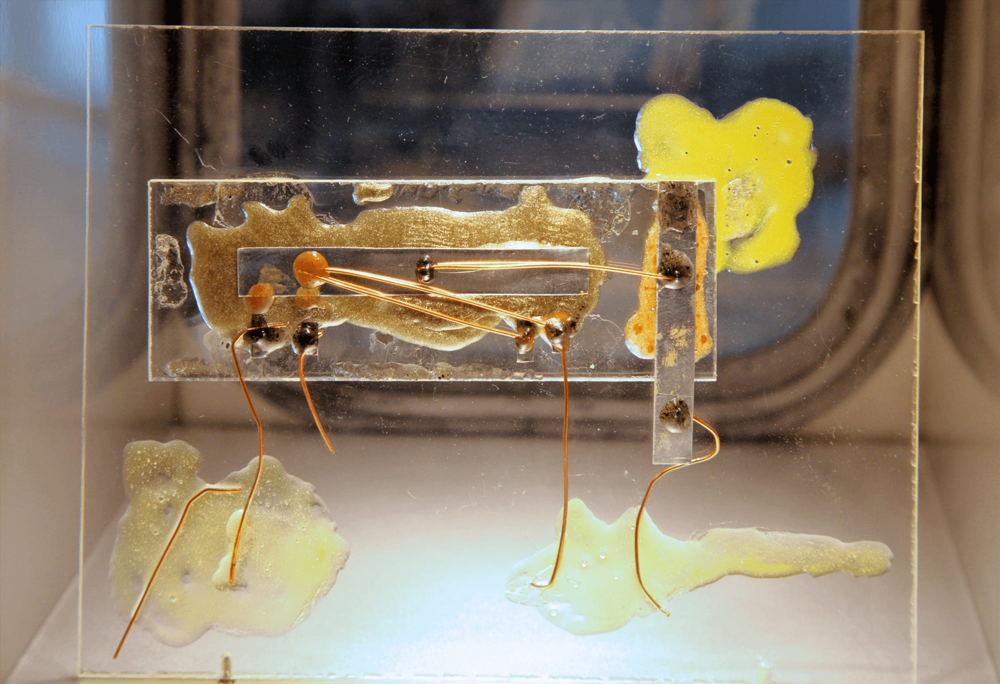 A replica of Kilby's first integrated circuit on a clear plate: a narrow strip, with thin gold-colored wires running across it and down from it.